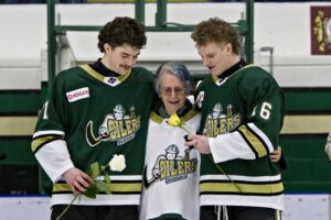 Cayden Joramo (left) and Joey Meredith (right) hand Oilers "Billet Grandma" Bev Lee (centre) flowers during Billet Appreciation Night. (Scott Savard/Okotoks Oilers)
